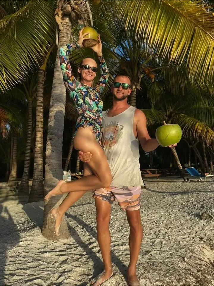 Hosts Szymon and Kamila on a Belize beach holding fresh coconuts under palm trees