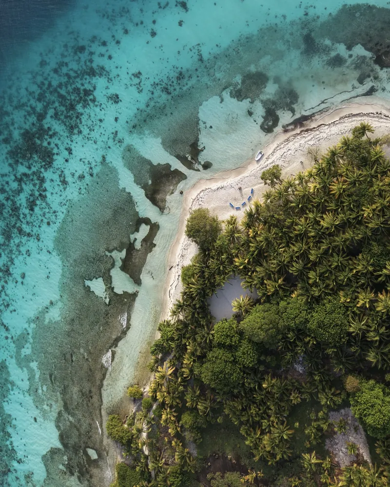 Aerial view of Moho Caye: palm forest, a white sand spit and shallow reef water